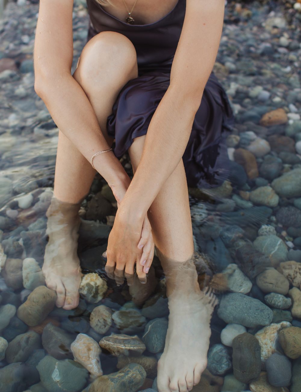 Woman in purple dress sitting in water over color pebbles